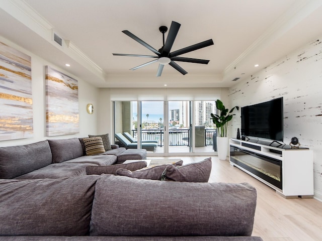 living room featuring a raised ceiling, light hardwood / wood-style flooring, and ornamental molding