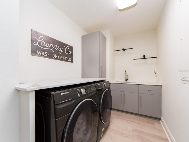 laundry area with washer and dryer, light wood-type flooring, cabinets, and sink