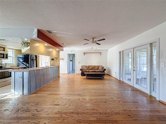 living room featuring french doors, sink, ceiling fan, a textured ceiling, and light hardwood / wood-style floors