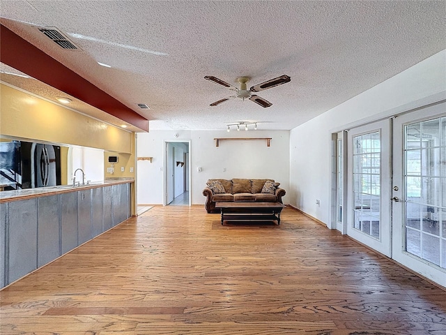 living room featuring ceiling fan, french doors, rail lighting, light hardwood / wood-style flooring, and a textured ceiling