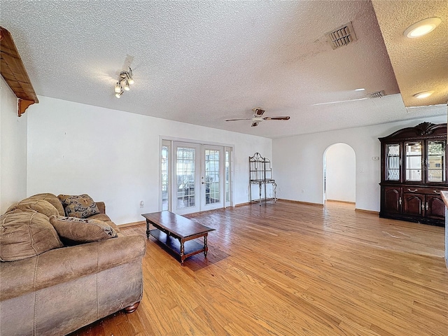 living room featuring ceiling fan, french doors, a textured ceiling, and light wood-type flooring