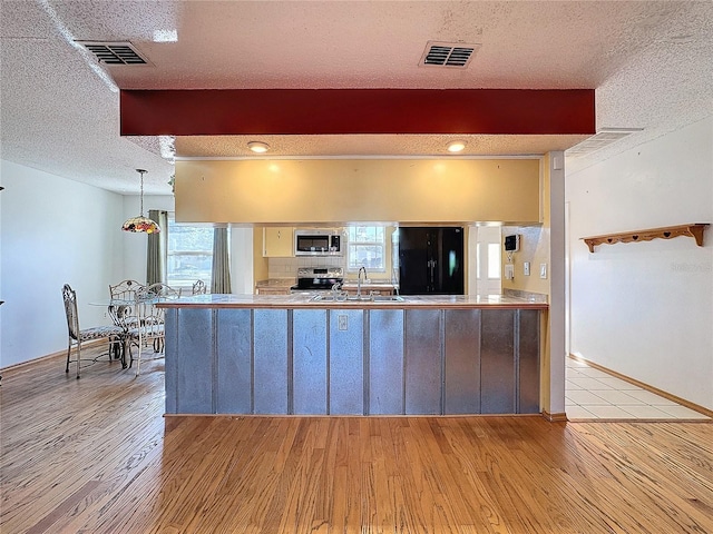 kitchen featuring sink, stainless steel appliances, pendant lighting, a textured ceiling, and light hardwood / wood-style floors