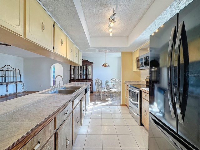 kitchen with pendant lighting, sink, rail lighting, appliances with stainless steel finishes, and a tray ceiling