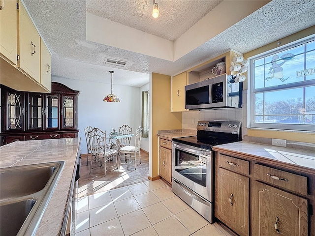 kitchen featuring stainless steel appliances, a raised ceiling, sink, decorative light fixtures, and light tile patterned flooring