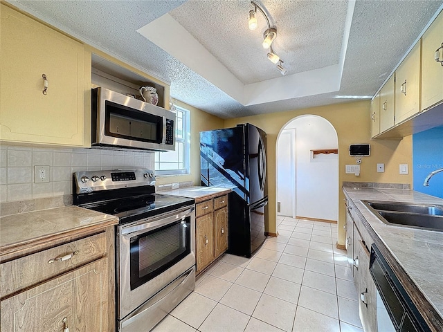 kitchen featuring sink, stainless steel appliances, track lighting, a tray ceiling, and light tile patterned flooring