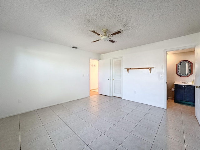 unfurnished bedroom with a textured ceiling, ceiling fan, light tile patterned flooring, and ensuite bathroom