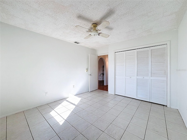 unfurnished bedroom with ceiling fan, a closet, light tile patterned floors, and a textured ceiling