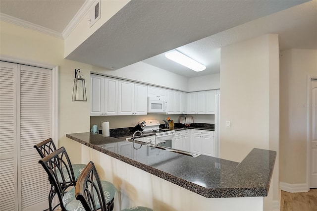 kitchen with a kitchen breakfast bar, kitchen peninsula, white cabinets, and white appliances