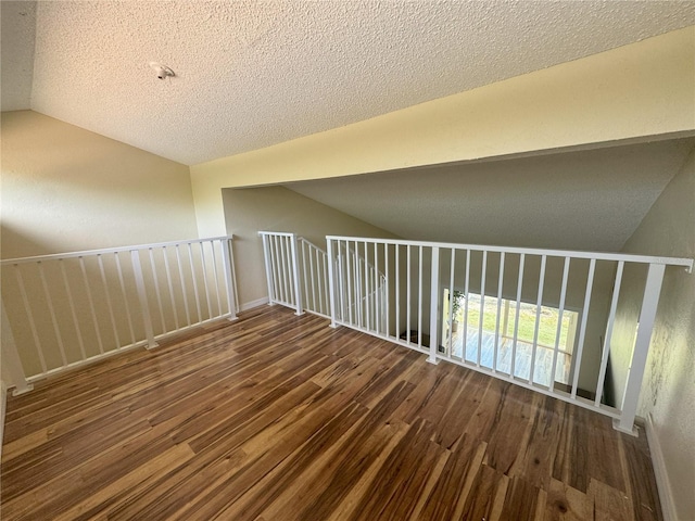 additional living space featuring vaulted ceiling, dark hardwood / wood-style flooring, and a textured ceiling