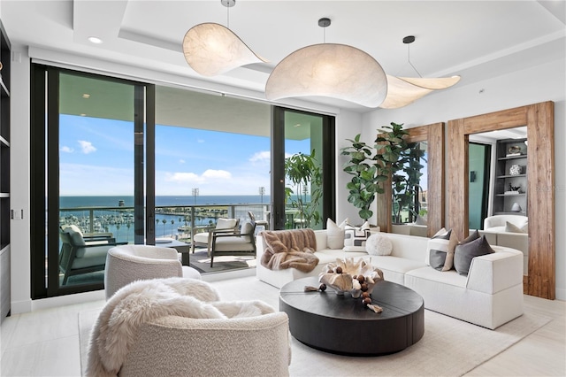 living room featuring a raised ceiling, a water view, a healthy amount of sunlight, and a wall of windows