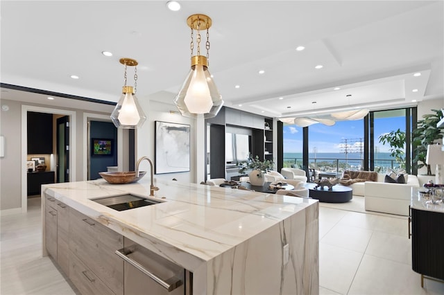 kitchen with a large island with sink, light stone counters, pendant lighting, and sink