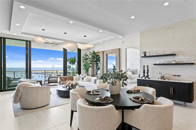 dining area featuring a water view, a raised ceiling, and expansive windows