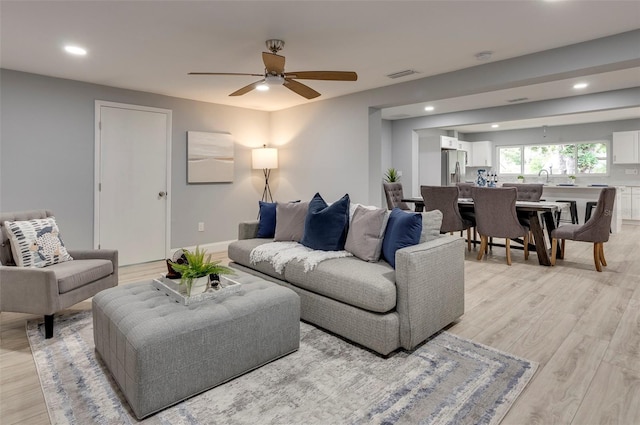 living room featuring ceiling fan, light wood-type flooring, and sink