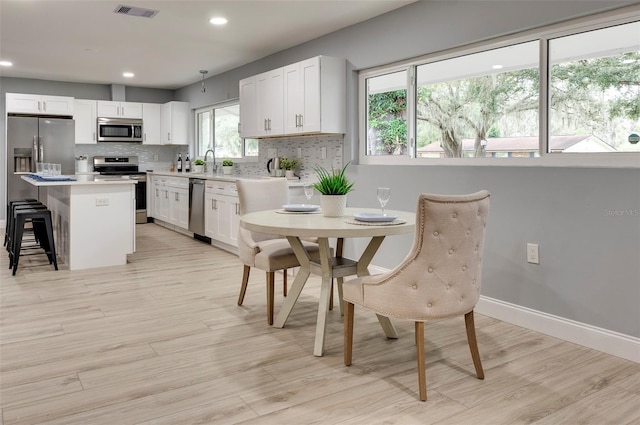 kitchen featuring appliances with stainless steel finishes, a center island, light hardwood / wood-style floors, white cabinetry, and a breakfast bar area