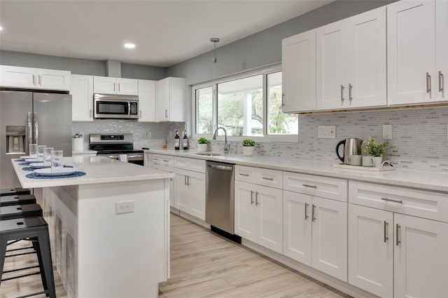 kitchen featuring tasteful backsplash, a kitchen island, light stone counters, white cabinetry, and stainless steel appliances