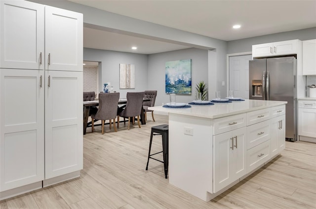 kitchen with white cabinets, stainless steel fridge, a kitchen bar, and a kitchen island