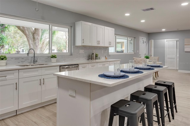 kitchen with sink, a kitchen island, stainless steel dishwasher, a breakfast bar area, and white cabinets