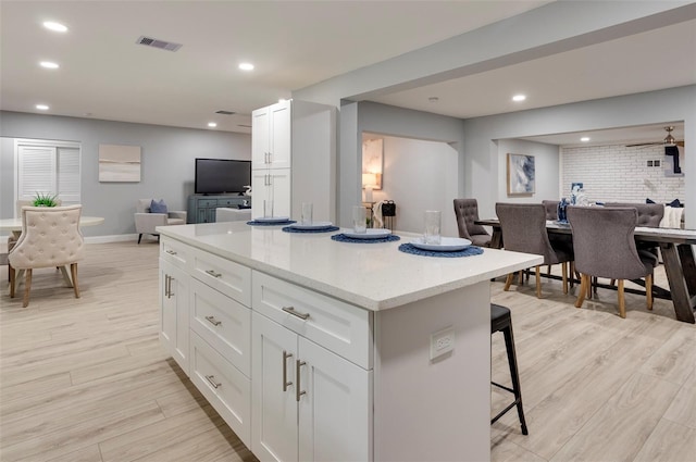 kitchen with a kitchen bar, light stone counters, brick wall, a kitchen island, and white cabinetry