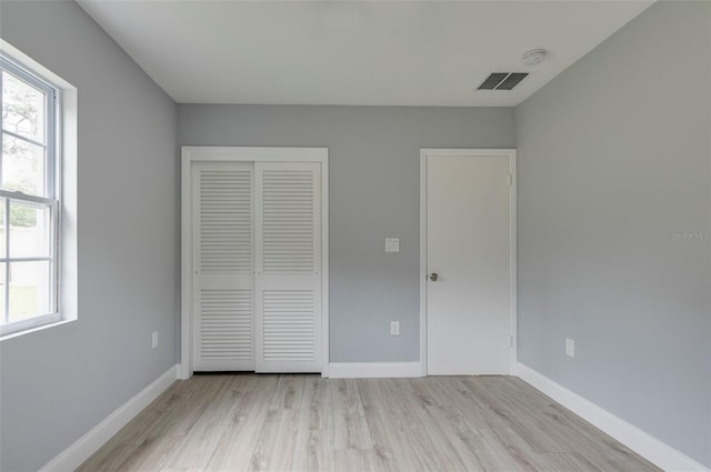 unfurnished bedroom featuring light wood-type flooring, a closet, and multiple windows