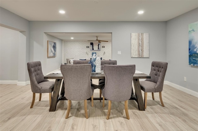 dining area with ceiling fan, light wood-type flooring, and brick wall