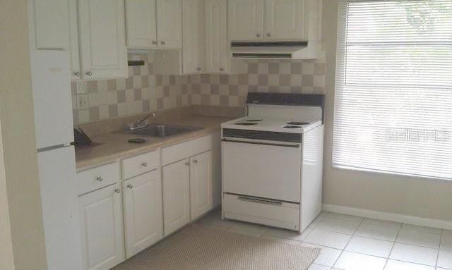 kitchen featuring light tile patterned flooring, tasteful backsplash, sink, white cabinets, and white appliances