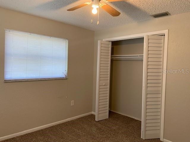 unfurnished bedroom featuring ceiling fan, a textured ceiling, a closet, and dark colored carpet