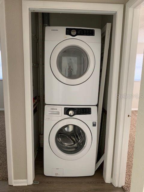 laundry room with dark wood-type flooring and stacked washing maching and dryer