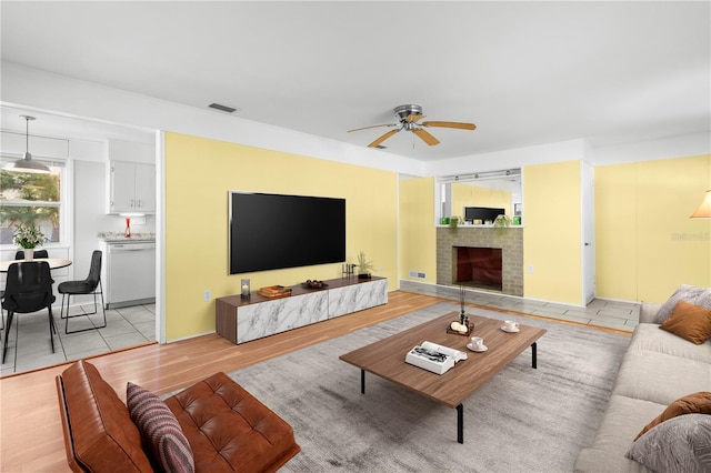 living room with ceiling fan, light hardwood / wood-style floors, and a brick fireplace