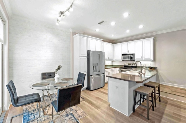 kitchen featuring sink, kitchen peninsula, a kitchen bar, white cabinetry, and stainless steel appliances