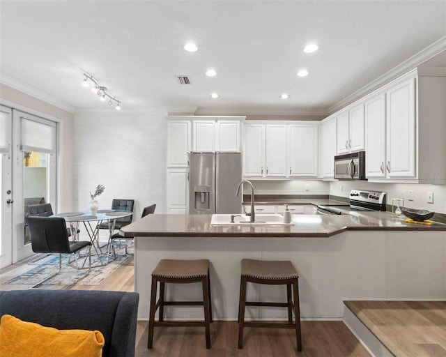 kitchen with sink, appliances with stainless steel finishes, a breakfast bar, white cabinets, and ornamental molding