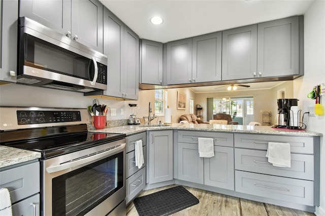 kitchen featuring gray cabinetry, light hardwood / wood-style flooring, ceiling fan, light stone countertops, and appliances with stainless steel finishes