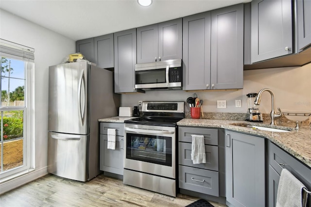 kitchen featuring sink, gray cabinets, light wood-type flooring, light stone counters, and stainless steel appliances