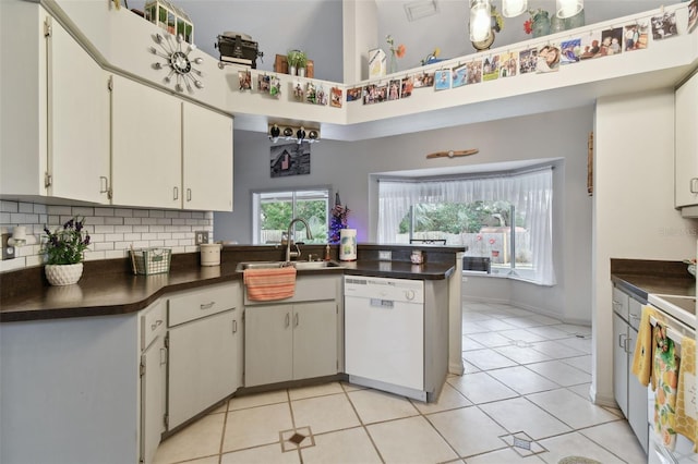 kitchen with dishwasher, a high ceiling, kitchen peninsula, decorative backsplash, and light tile patterned floors