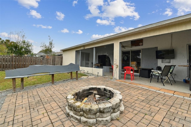 view of patio / terrace with a fire pit, ceiling fan, and a sunroom