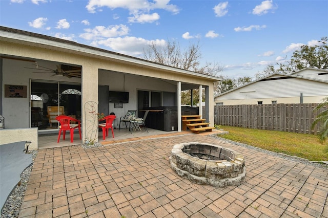 view of patio with ceiling fan, a hot tub, and an outdoor fire pit