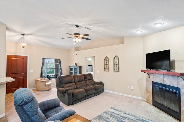 living room featuring a textured ceiling, vaulted ceiling, ceiling fan, light colored carpet, and a tiled fireplace