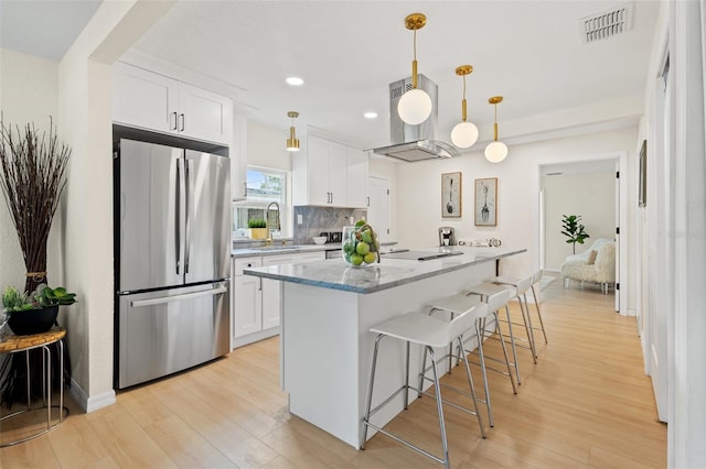 kitchen featuring light stone countertops, backsplash, white cabinets, a center island, and stainless steel refrigerator