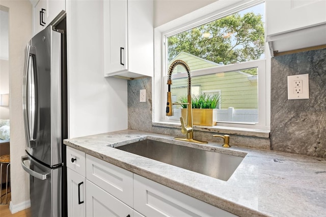 kitchen featuring stainless steel fridge, sink, white cabinets, and light stone counters