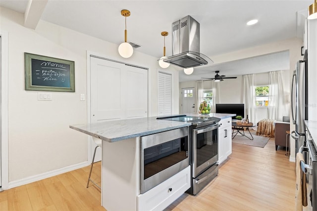 kitchen featuring stainless steel electric stove, decorative light fixtures, a breakfast bar area, island range hood, and white cabinets