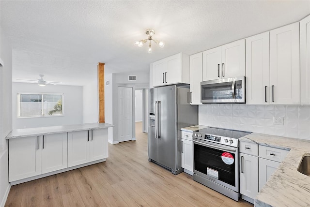 kitchen with light stone countertops, appliances with stainless steel finishes, tasteful backsplash, ceiling fan with notable chandelier, and white cabinets