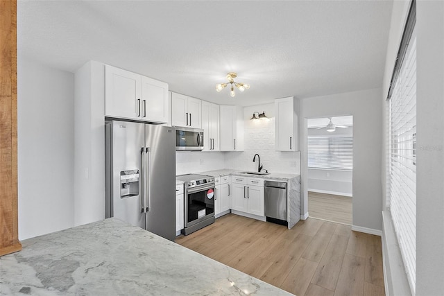 kitchen with white cabinetry, sink, stainless steel appliances, ceiling fan with notable chandelier, and light wood-type flooring