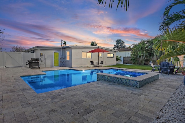 pool at dusk with an in ground hot tub, grilling area, and a patio area