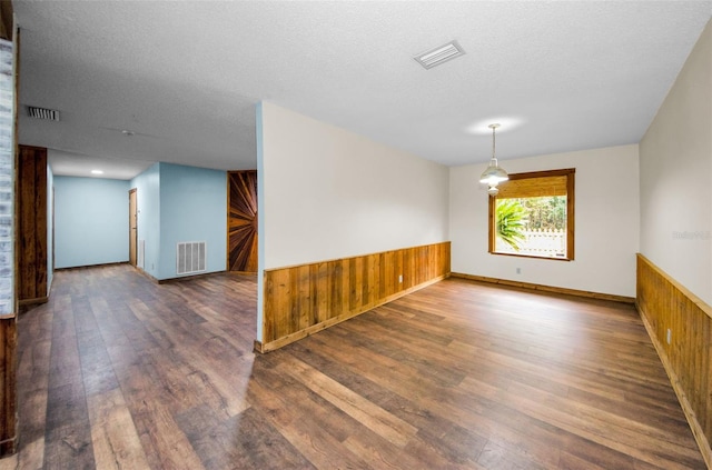 empty room with wood walls, dark hardwood / wood-style floors, and a textured ceiling