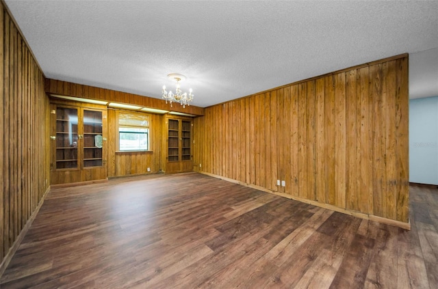 spare room with wood walls, dark wood-type flooring, a chandelier, and a textured ceiling