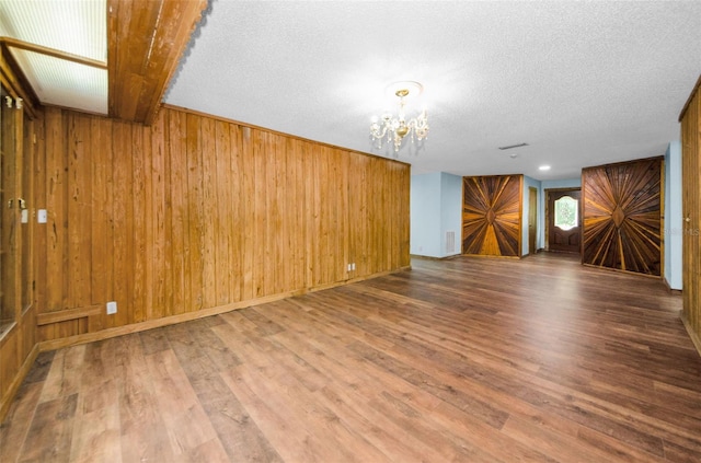 spare room with wooden walls, a chandelier, a textured ceiling, and wood-type flooring