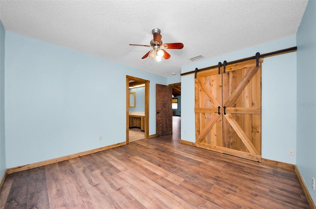 unfurnished bedroom with ensuite bath, ceiling fan, a barn door, a textured ceiling, and wood-type flooring