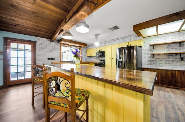 kitchen with a breakfast bar area, butcher block counters, stainless steel appliances, and brick wall