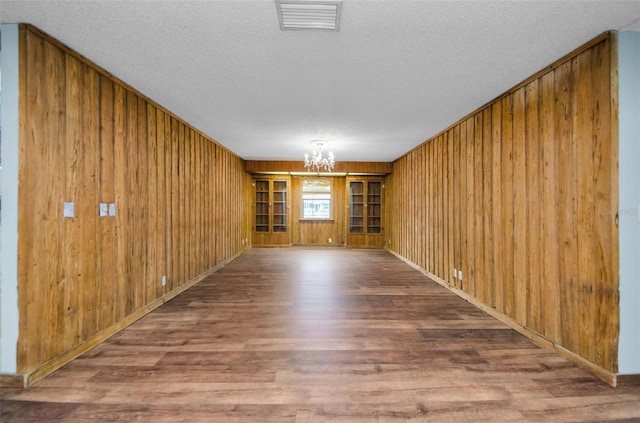 empty room featuring hardwood / wood-style flooring, wood walls, a textured ceiling, and an inviting chandelier