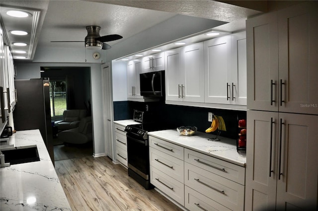 kitchen featuring light stone countertops, light hardwood / wood-style floors, white cabinetry, and black appliances