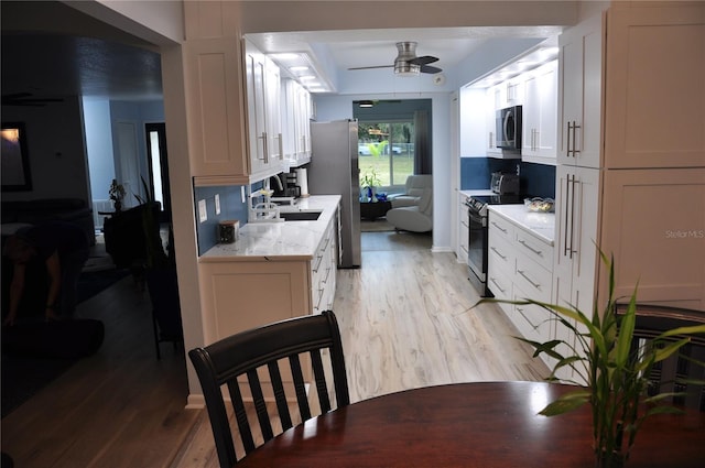 kitchen with stainless steel appliances, white cabinetry, ceiling fan, and light hardwood / wood-style flooring